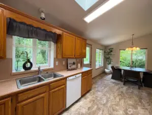 Galley-style kitchen with oak cabinetry, garden window over the sink, and serene backyard views.