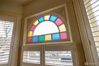 Colorful arched stained-glass transom window framed by detailed Victorian trim.