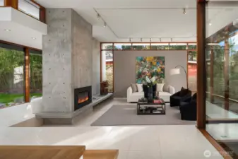 Just beyond, an intentional glimpse reveals the sunken living room—a subtle nod to mid-century design—anchored by a sculptural concrete fireplace with a linear gas insert and extended bench hearth.