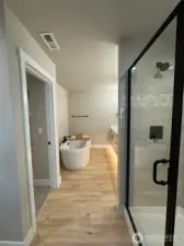 Primary bathroom with tiled shower, soaking tub, walk in closet, quartz countertop, & undercabinet lighting