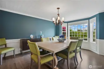 Designed for both everyday gatherings and special occasions, this refined dining space blends timeless details with modern comfort. Wainscoting adds depth and character, complemented by crown molding and high ceilings that enhance the room’s spacious feel. A statement chandelier casts a warm glow over the central dining area, while large windows invite natural light, framed by sophisticated window treatments for added elegance. Whether hosting intimate dinners or festive celebrations, this beautifully appointed space offers a perfect balance of style and functionality.
