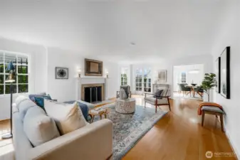 Spacious living room with oak floors, a classic wood-burning fireplace, and abundant light from southeast-facing windows and French doors that open to the private backyard patio.