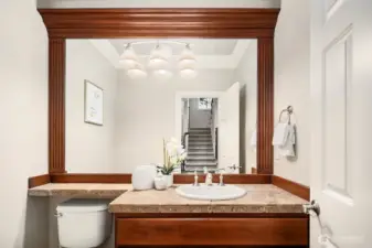 The elegant powder room makes a lasting impression with its rich wood vanity, warm granite countertop, and a beautifully framed mirror that adds a refined, finishing touch. This thoughtfully appointed space perfectly reflects the quality and attention to detail found throughout the entire home.