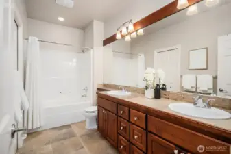 The well-appointed hall bath serves the secondary bedrooms with style and functionality, featuring a rich wood vanity with dual sinks, generous counter space, and a clean, classic tile surround tub and shower combination. Warm finishes and thoughtful details make this a bathroom that comfortably accommodates the needs of family and guests alike.