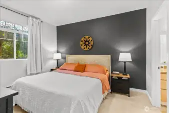 The spacious primary suite features soft neutral carpeting, a large window for natural light, and direct access to a private bathroom.