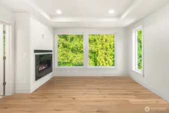 Serene greenbelt backing primary with contemporary linear fireplace with custom slab surround and steel mantel
