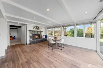 Expansive lower-level family room with luxury vinyl plank flooring and a wall of windows bringing in natural light. A gas fireplace with stone surround anchors the space, creating a warm focal point for gathering.