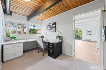 Dedicated workspace with built-in desk, expansive counter surface, and large windows for natural light. Wood ceiling with exposed beams adds character, creating an inspiring setting for work or study.