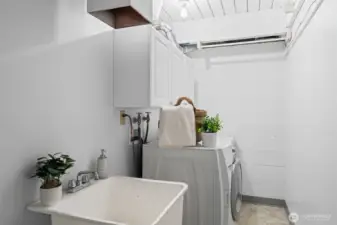 Functional lower-level utility space with washer and dryer, utility sink, and overhead storage. Practical layout offers room for laundry tasks, storage, and household organization.