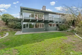 Spacious backyard with lush lawn and beautifully landscaped borders, complemented by an expansive deck above—ideal for outdoor living, entertaining, and enjoying the peaceful setting.