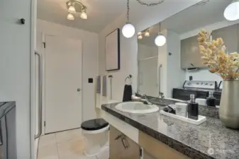 This bathroom with granite tile counter top, tile flooring, and newer toilet also functions as the laundry room.