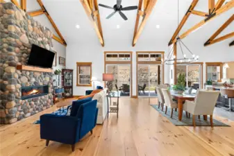 View 2 of the Living Room with soaring ceilings, exposed wood beams, wide plank wood floors, stone fireplace and glass sliding doors leading to the outdoor living area.