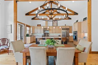 View 1 of the Dining Room with soaring ceilings, exposed wood beams, wide plank wood floors, stone fireplace and glass sliding doors leading to the outdoor living area.