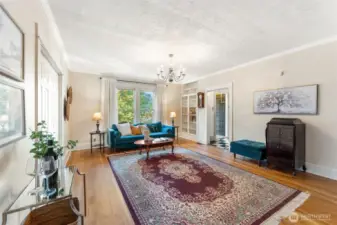 Open living room with expansive windows, chandelier lighting, and views of the surrounding greenery.