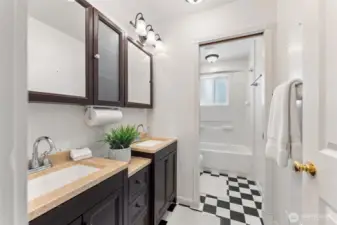 Updated main floor bathroom with dual sinks, rich cabinetry, and classic black-and-white flooring.