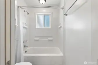 Bright bathroom with a tiled shower and tub combo, window for natural light, and timeless white finishes.