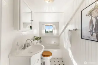Bright upstairs bathroom with white beadboard walls, a tub/shower combo, and natural light from a large window.