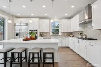 Gourmet kitchen featuring an expansive island, quartz countertops, 48" counter depth refrigerator, gas cooktop and built-in microwave and oven. Designed for both everyday living and entertaining. Showing another staged home in the community, white cabinetry is an upgrade.