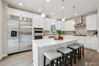 Gourmet kitchen featuring an expansive island, quartz countertops, 48" counter depth refrigerator, gas cooktop and built-in microwave and oven. Designed for both everyday living and entertaining.  Showing another staged home in the community, white cabinetry is an upgrade.