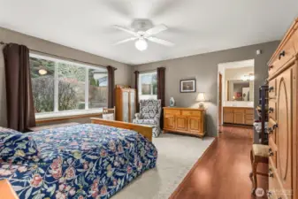 Lovely view from the primary bedroom. Soft Carpeted flooring surrounds the bed area with warm walnut flooring leading to the bathroom. Walk-in closet to the right.