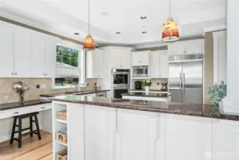This spacious kitchen features abundant cabinetry, recessed and pendant lighting, quality stainless appliances, a desk area, and lake and mountain views.