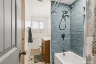 Meticulously maintained Des Moines home full bathroom, featuring striking glazed blue subway tile surrounds and a high-end contemporary rain shower system, perfectly complimented by a rich wood vanity and newer fixtures.