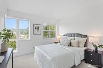 The spacious primary bedroom with a wall of windows looks out to lush green space and territorial views.