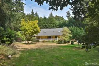 Western view of your home. Charming covered front porch wraps from the main entrance (north side of house) along the entire western side of your home. Note the skylights (one in the living room and one in the kitchen).