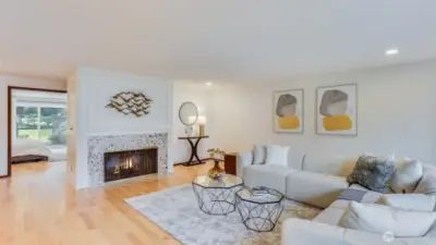 Step inside to this spacious and bright living room with gleaming hardwood floors, wood burning fireplace and a wall of windows, showcasing serene nature views.