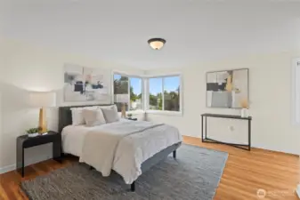 Upstairs the primary bedroom has original hardwood floors and corner windows with a partial view of Commencement Bay