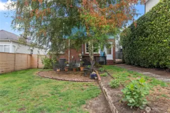 A garden-like backyard with a brick patio and mature hedges.