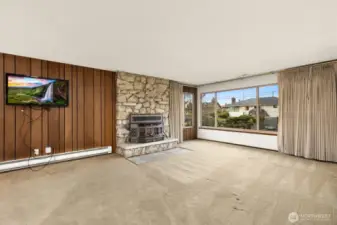 Living room features corner window offering wonderful light, and wood fireplace insert. Stone chimney facade and wood paneling.  Installed TV's stay with home.