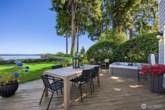 Spacious deck with outdoor dining area and hot tub, overlooking the lawn and expansive water views - ideal for relaxing or entertaining.