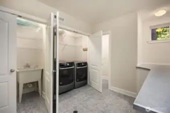 Downstairs dedicated laundry room with utility sink, front-loading washer and dryer, built-in shelving, and folding counter for added convenience. Connected to a half bath as well.