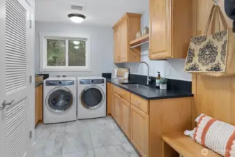 Utility room with sink and built in bench/storage/hanging hooks + closet. The black quartz extends throughout the home, including here.
