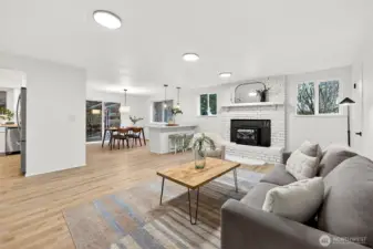 A wide-angle view captures the seamless flow from the family room with brick fireplace through to the dining area and kitchen beyond, showcasing the home's open and connected layout.