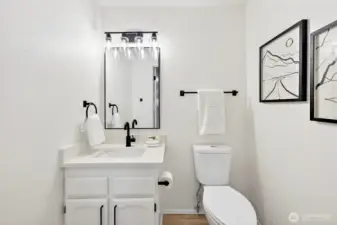 A crisp, updated bath features a white quartz vanity, matte black fixtures, framed mirror, and globe vanity lighting — clean and polished from top to bottom.