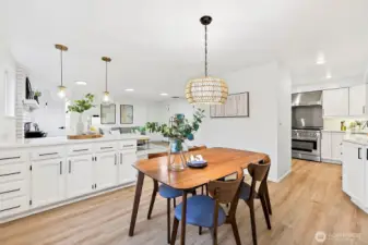 A second angle highlights the dining room's connection to the kitchen, with a woven chandelier overhead, white cabinetry lining the wall, and a clear sightline to the professional-grade range.