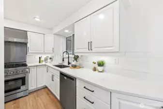 The updated kitchen features white raised-panel cabinetry with matte black hardware, quartz countertops, subway tile backsplash, and stainless steel appliances including a professional gas range.