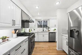 A full view of the galley-style kitchen showcases the pro-grade gas range with stainless hood, built-in dishwasher, deep sink with black gooseneck faucet, and generous counter space throughout.