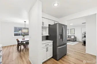 The stainless French door refrigerator anchors the kitchen's main wall, with built-in open shelving above and a clear sightline through to the dining room and family room beyond.