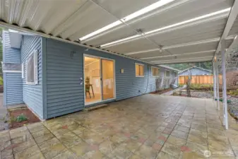 The expansive covered patio with translucent roofing and stone tile flooring stretches the full width of the home, accessible via a sliding glass door — a true all-weather outdoor living space.