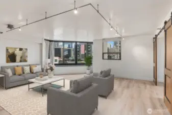Virtually staged Seattle condo living area showcasing an open layout, modern track lighting, and large windows overlooking surrounding downtown buildings.