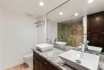 Seattle condo bathroom with dual vessel sinks, large vanity with ample counter space, full mirror wall, and glass shower with tiled surround.