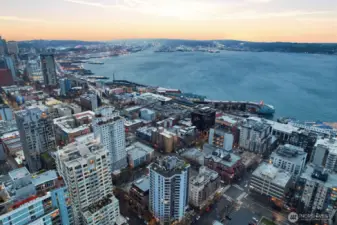 Belltown Seattle aerial view overlooking Elliott Bay with working waterfront activity, cargo terminals, and surrounding downtown Seattle skyline at sunset.