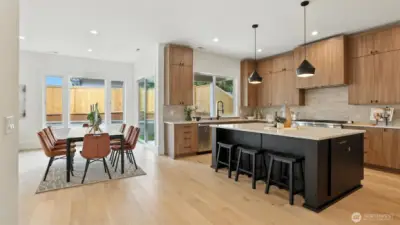 Designed for the way people truly live — connected, open, and beautifully balanced. The kitchen showcases full-height cabinetry, quartz counters, and a striking black island with informal seating. Pendant lighting adds architectural polish, while expansive windows flood the space with natural light. Adjacent, the dining area feels warm and modern, anchored by warm floors and a wall of glass that opens to the backyard — creating seamless indoor-outdoor flow for entertaining and everyday living.