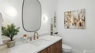 A statement in understated luxury, the powder bath features a marble-inspired countertop, warm brass colored fixtures, and designer lighting that adds sculptural interest. It’s a refined touchpoint for guests that reflects the home’s cohesive design vision.