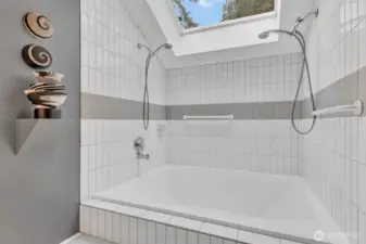 Primary bath is anchored by oversized soaking tub with dual shower heads, all drenched in light from large overhead skylight