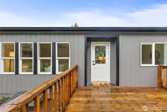 The front deck showcases a charming white entry door with glass panel and a "hello" doormat, framed by fresh board-and-batten siding with black accents.