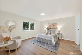 A peaceful primary suite with LVP flooring, a large window with yard views, recessed lighting, and a generous layout with sitting area.